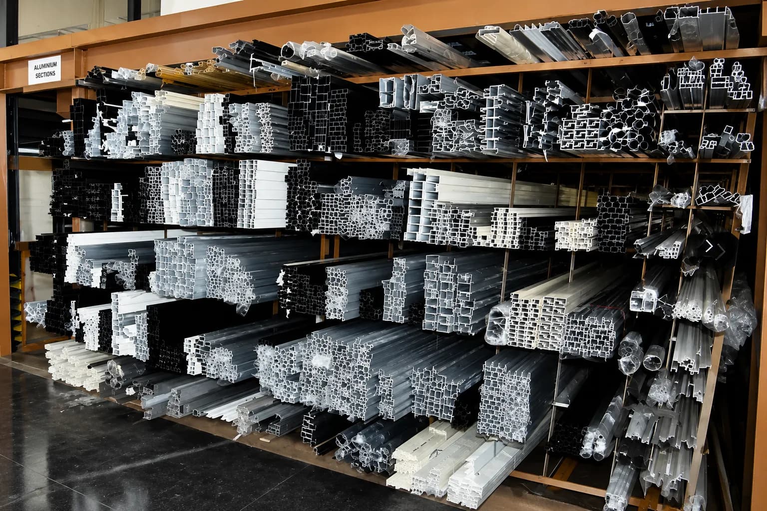 Assorted aluminium profile sections racked and sorted by shape on warehouse shelving